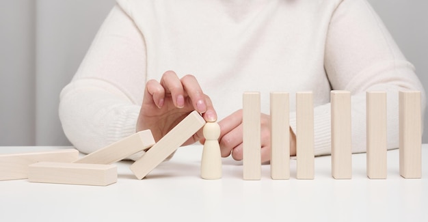 Main arrête la chute de figurines en bois d'hommes sur fond blanc Concept d'une personnalité forte et courageuse capable de résister à des difficultés inégales