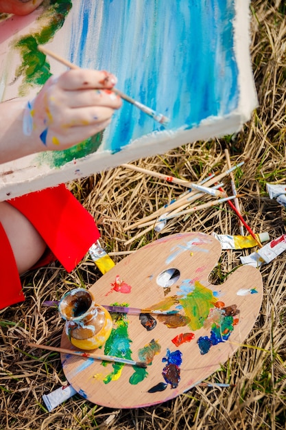 Main de l'artiste dessinant l'image et la palette avec des peintures et des pinceaux sur fond d'herbe.