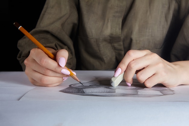 La main de l'artiste tient un gros plan au crayon et à la gomme.