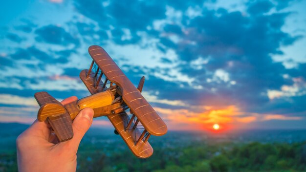 La main avec un avion jouet sur fond de lever de soleil