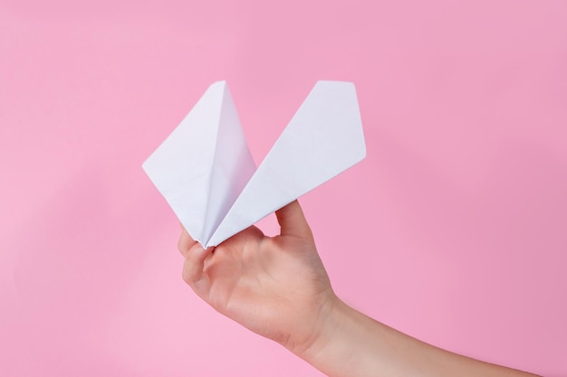 Main et avion en papier sur fond rose enfant joue