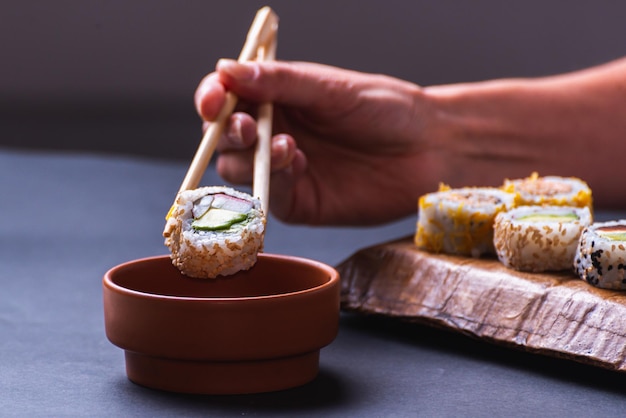 Main avec des baguettes trempant des sushis dans de la sauce soja