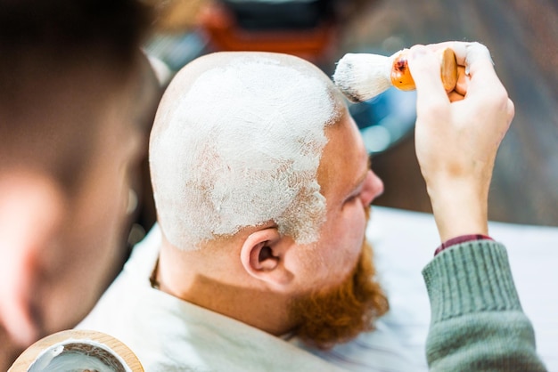 La main d'un barbier garde un blaireau crémeux au-dessus de la tête du client