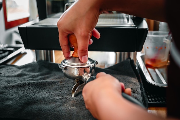 Main d'un barista tenant un porte-filtre et un bourreur de café faisant un café expresso