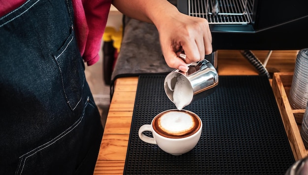 Photo la main d'un barista versant du lait dans le café pour faire du cappuccino un barista professionnel préparant du café