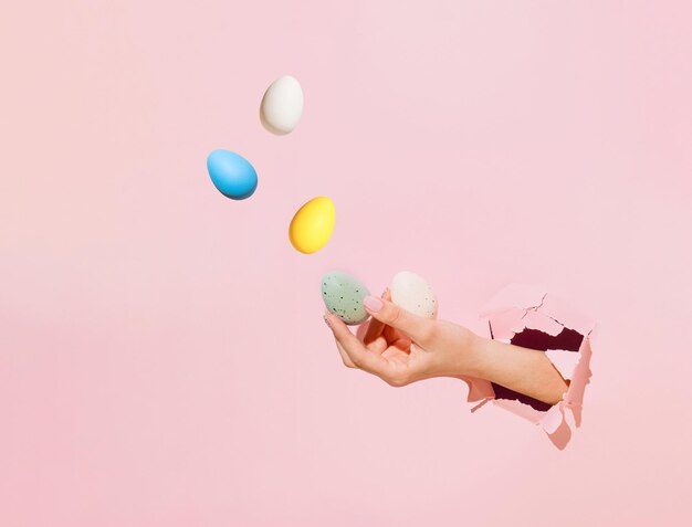 Main de belle femme jonglant avec des oeufs de Pâques papier déchiré rose espace de copie de concept de vacances minimal