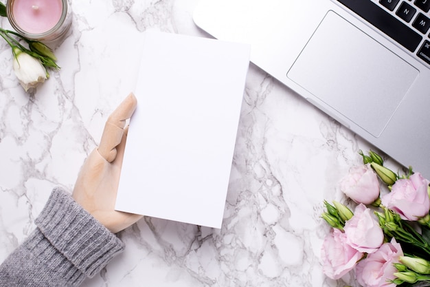 Main en bois avec carte présente blanche sur table de bureau en marbre avec fleurs roses