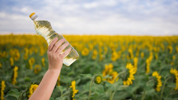 Une main avec une bouteille d'huile de tournesol dorée soulevée dans le contexte d'un champ de tournesols en fleurs dans un espace de copie ensoleillé