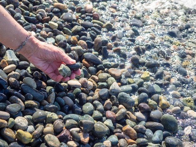 Photo une main avec un bracelet fait de pierres tient un caillou près de l'eau vague de mer et main féminine sentez la vague plage de galets