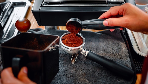 La main de la cafetière tenant une cuillère versant du moulin à poudre de café meulant du café versant