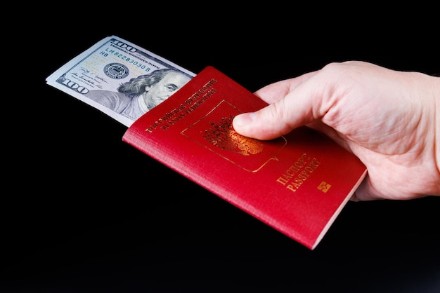 Main caucasienne tenant un passeport international russe avec des dollars américains insérés