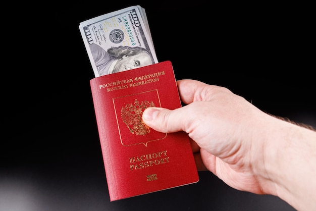 Main caucasienne tenant un passeport international russe avec des dollars américains insérés