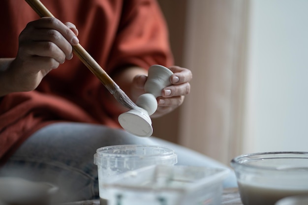 Main de céramiste femme utilisant un pinceau pour peindre les détails faisant de la poterie d'argile naturelle pour la préparation de la vente