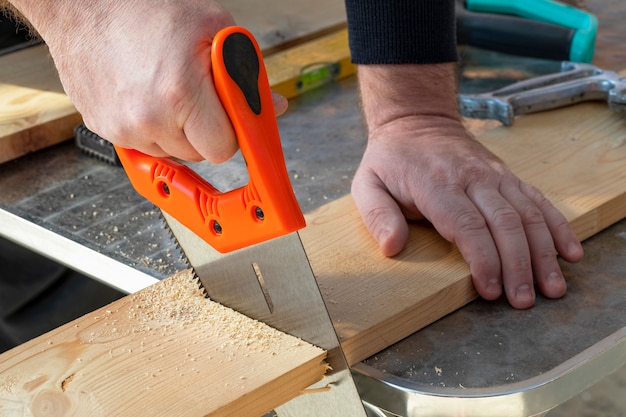 Main de charpentier avec scie à main, découpe de planches en bois.