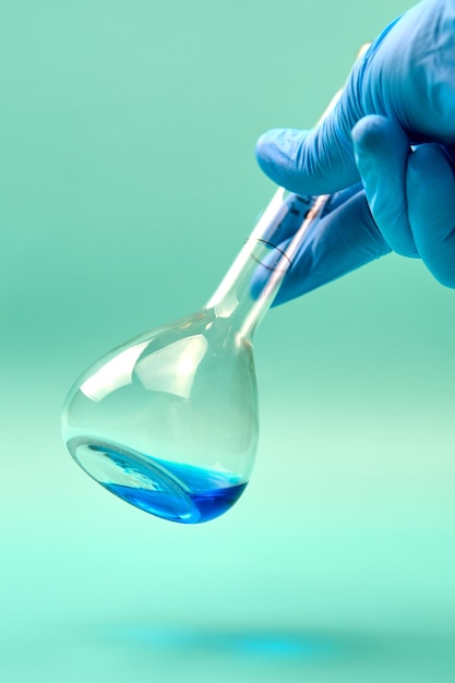 Photo main d'un chercheur non reconnaissable dans un gant de latex tenant un flacon de titration de substance chimique bleue pendant une expérience en laboratoire