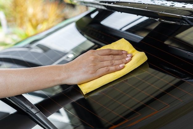 Main avec un chiffon en microfibre nettoyant la lunette arrière de la voiture