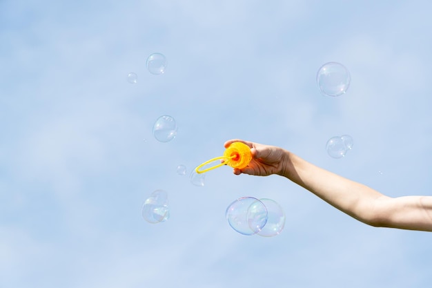 La main de Childs tenant une baguette pour souffler des bulles de savon contre le ciel bleu par une journée d'été ensoleillée