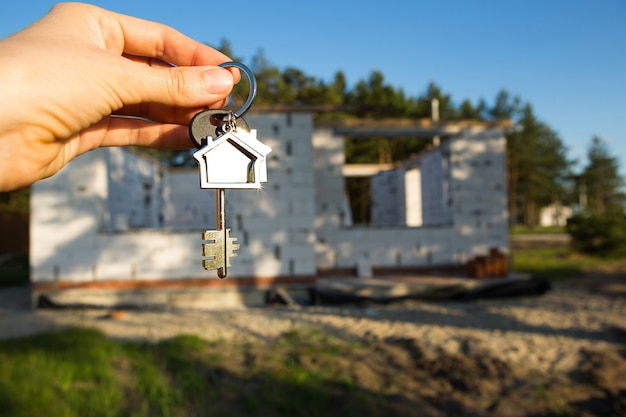 Main avec la clé de la future maison sur fond de chantier et murs en blocs de béton poreux. Construire une maison, déménager dans un nouveau chalet, ferme à la campagne