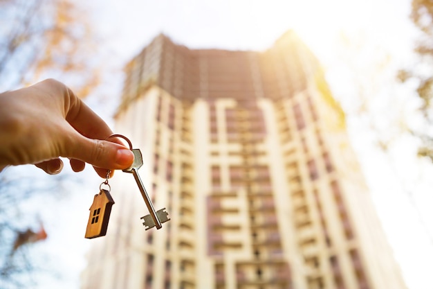 Main avec une clé et un porte-clés en bois. Fond de gratte-ciel à plusieurs appartements. Construire, déménager dans un nouvel appartement, hypothéquer, louer et acheter un bien immobilier. Pour ouvrir la porte. Espace de copie