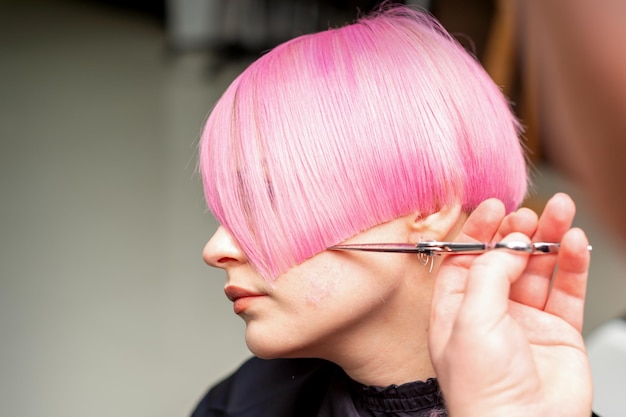 Main d'un coiffeur coupe courte rose avec des cheveux en ciseaux dans un salon de coiffure vue rapprochée