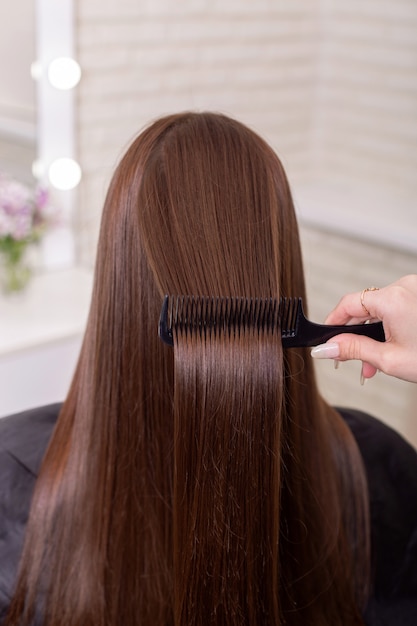 Main de coiffeurs brossant de longs cheveux bruns dans un salon de beauté