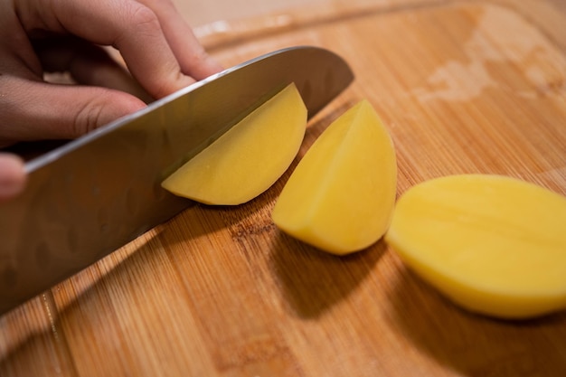 Photo une main coupe des pommes de terre crues avec un couteau en métal pour cuisiner une préparation alimentaire saine