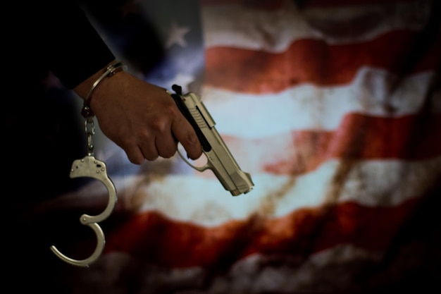 Photo la main coupée d'un criminel tenant une arme contre le drapeau américain
