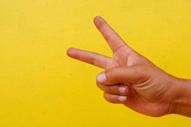 Photo la main coupée fait un signe de paix contre le mur jaune.