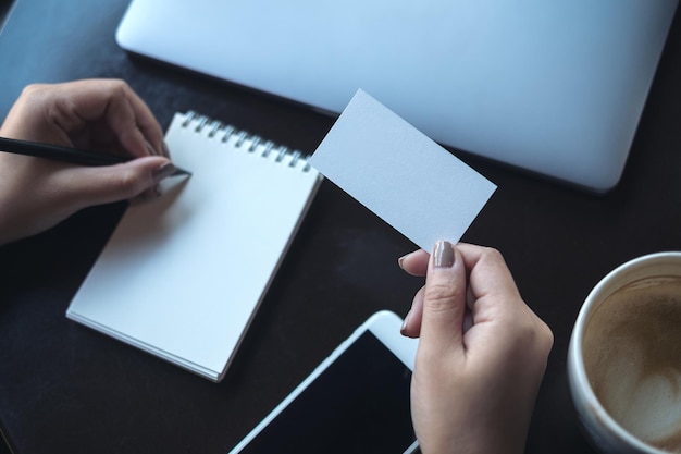 Main coupée d'une femme d'affaires écrivant sur un bloc-notes tout en tenant un papier blanc au bureau