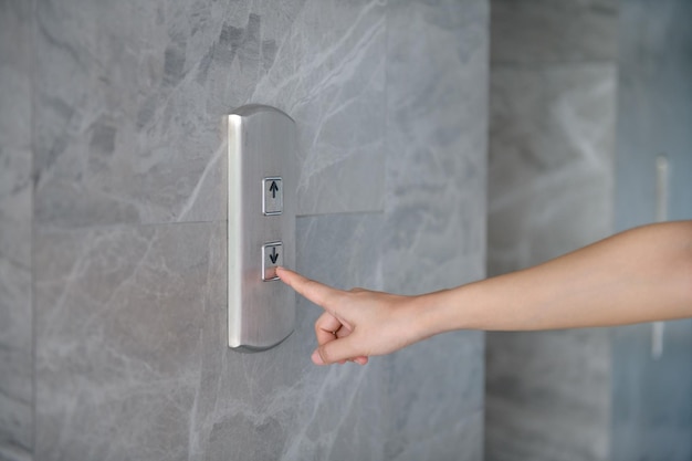 La main coupée de la femme en appuyant sur le bouton poussoir pour l'ascenseur sur le mur