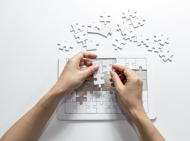 Main coupée d'une femme attachant des pièces de puzzle sur un fond blanc