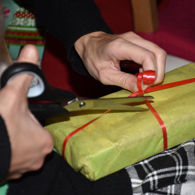 Photo main coupée d'une femme coupant un ruban de cadeau sur la table