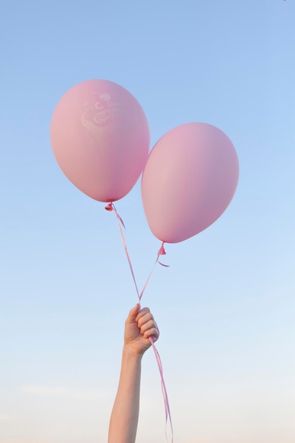 La main coupée d'une femme tenant des ballons contre un ciel clair