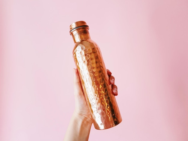 Photo la main coupée d'une femme tenant une bouteille contre le mur