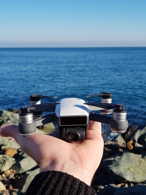 Photo la main coupée d'une femme tenant un drone sur la plage contre un ciel clair