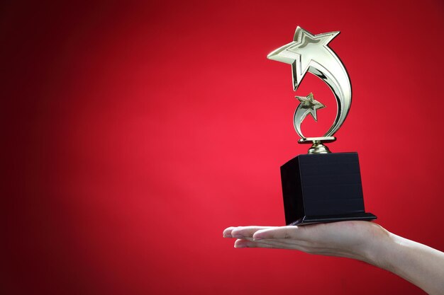 Photo main coupée d'une femme tenant un trophée sur fond rouge