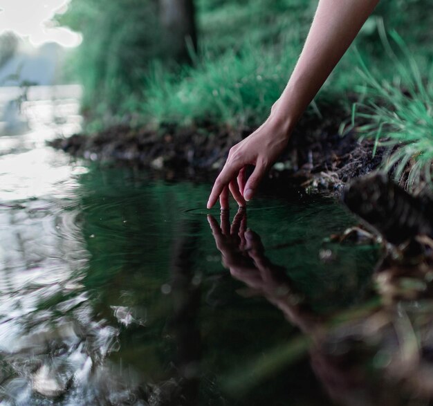 Photo main coupée d'une femme touchant l'eau dans un lac