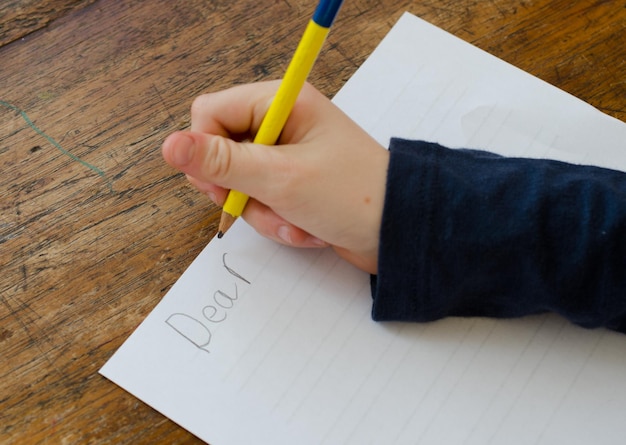 La main coupée d'une fille écrivant dans le papier sur la table