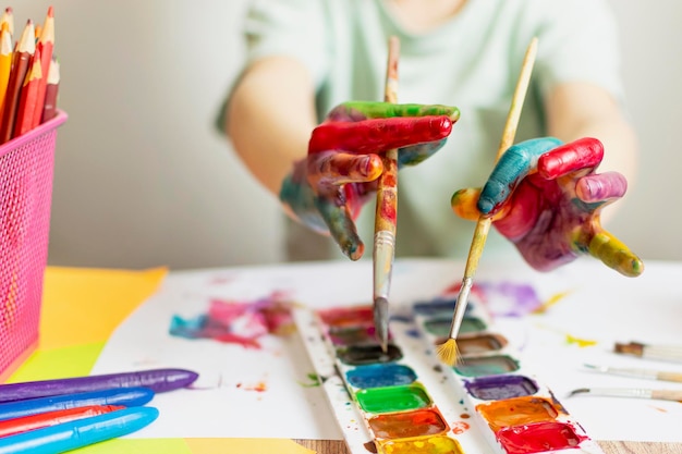 Main coupée d'un garçon tenant un pinceau sur la palette alors qu'il peint en classe