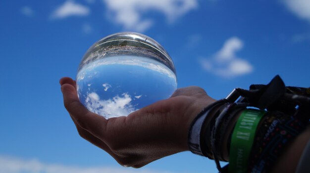 Photo la main coupée d'un homme tenant une boule de cristal contre le ciel bleu