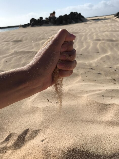 Photo main coupée d'un homme tenant du sable sur la plage