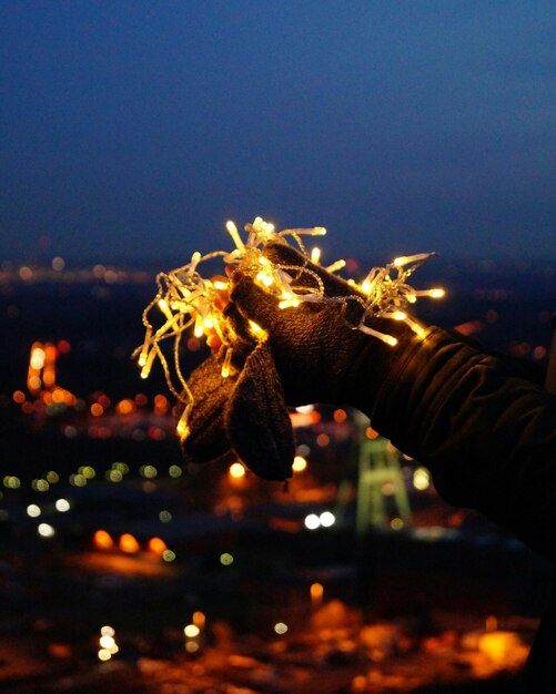 Photo la main coupée d'un homme tenant des lumières éclairées contre la ville la nuit