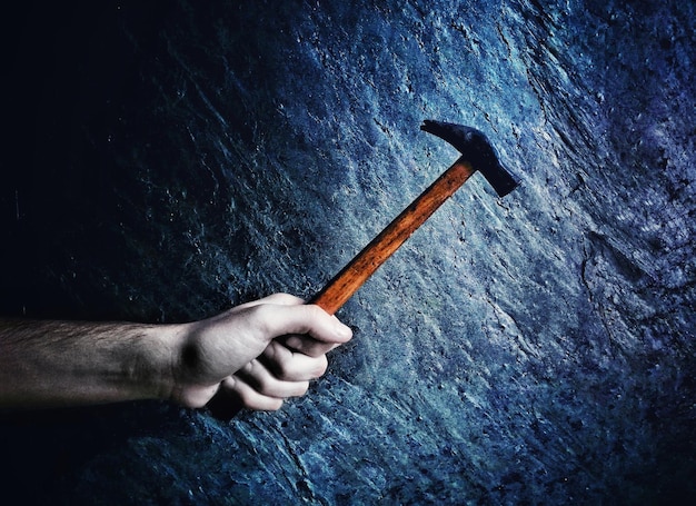 Photo main coupée d'un homme tenant un marteau contre le mur