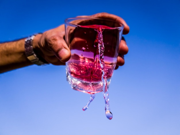 La main coupée d'un homme versant de la boisson dans un verre contre un ciel bleu clair