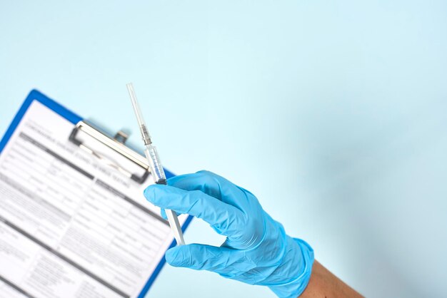 Photo main coupée d'un médecin tenant une seringue sur un fond bleu