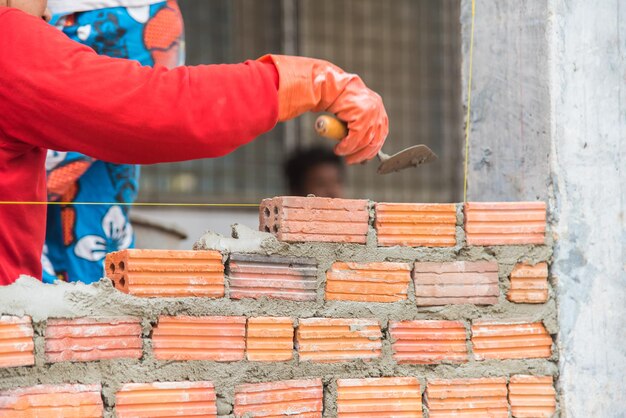 Photo main coupée d'un ouvrier fabriquant un mur de briques sur un chantier de construction