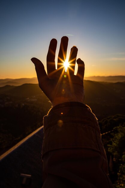 Photo main coupée d'une personne contre le soleil au coucher du soleil