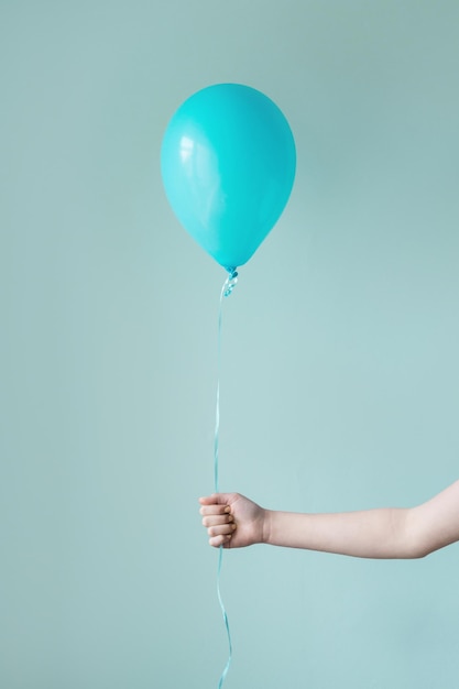 Photo main coupée d'une personne tenant un ballon sur un fond turquoise