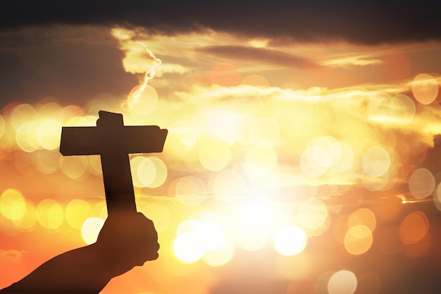 Main coupée d'une personne tenant une croix contre le ciel au coucher du soleil