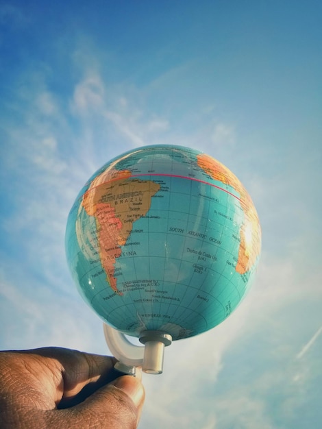 Main coupée d'une personne tenant un globe contre le ciel
